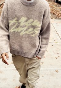 Vaaleanharmaa villapaita pehmeällä tekstuurilla, jossa on haalistunut keltainen graafinen kuvio. Yhdistetty beigenväristen puuvillafarkkujen kanssa.