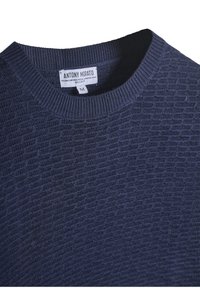Marineblauwe crewneck trui gemaakt van gestructureerde merino wol met geribde mouwen. Etiket zichtbaar met merknaam en maatinformatie.