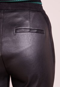 Svarta läderbyxor med en slät yta, snitt som sitter tajt och en enda bakficka med en stilren horisontell öppning.