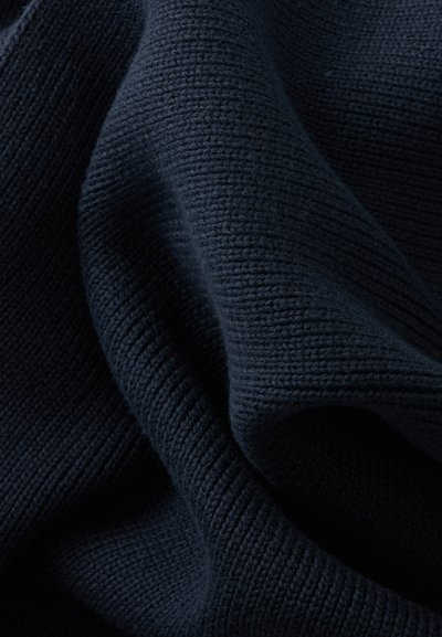 Gros plan d'un tissu tricoté bleu marine foncé montrant un motif côtelé doux et texturé ainsi que des plis délicats.