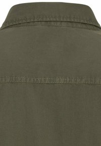 Chemise vert olive en tissu texturé. Dispose d'un col classique et de coutures horizontales détaillées au dos. Design simple, sans motifs visibles.