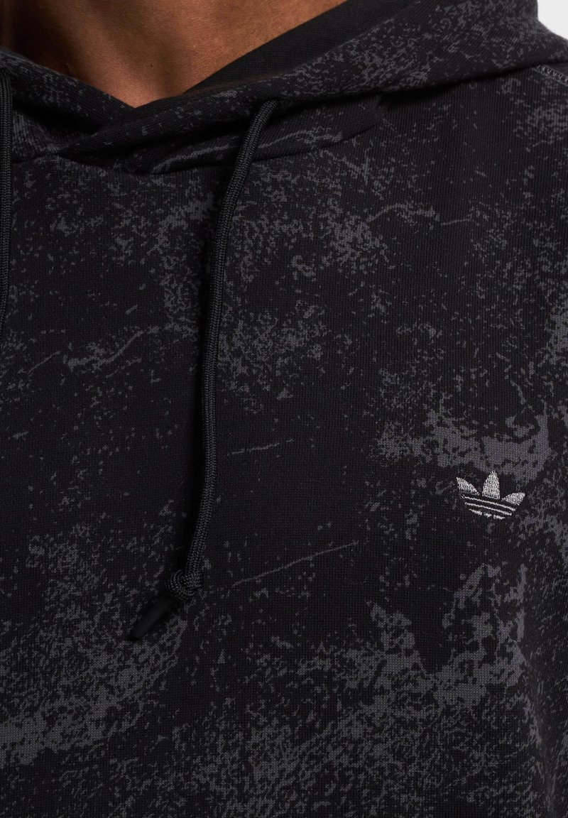 Schwarzer Hoodie mit strukturiertem Muster und grauen Akzenten. Mit Kordeln am Ausschnitt und einem kleinen silbernen Logo auf der Brust.