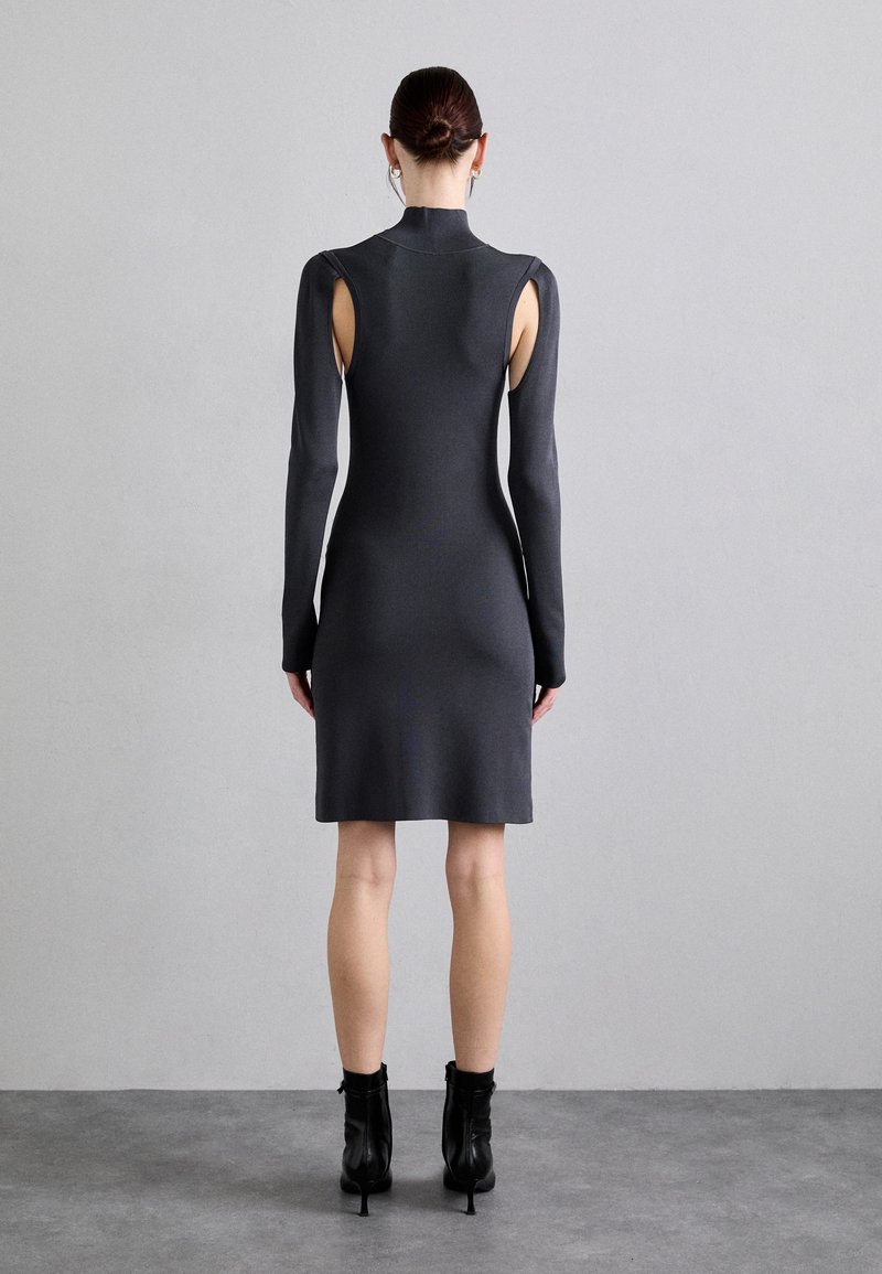 Strak aansluitende jurk met lange mouwen van donkergrijs geribbeld materiaal, met uitsparingen op de schouders en een hoge halslijn. Eindigt net boven de knieën.