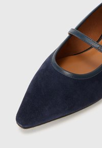 Scarpa piatta in suede blu navy con punta affusolata e una sottile fascia sul collo del piede, caratterizzata da un bordo in pelle liscia attorno all'apertura.