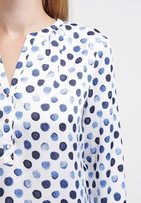Blusa bianca con una patta dei bottoni, con un motivo di pois blu e blu navy; tessuto leggero con una finitura strutturata.