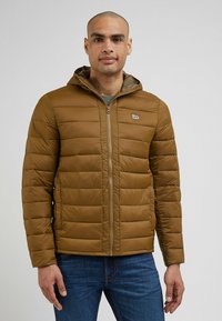Brązowa kurtka ocieplana z kapturem, z poziomymi przeszyciami i zapięciem na zamek. Małe logo na lewej piersi i ściśnięte mankiety.