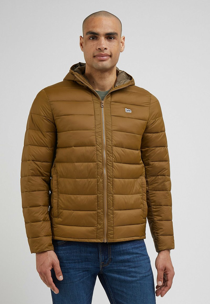 Brązowa kurtka ocieplana z kapturem, z poziomymi przeszyciami i zapięciem na zamek. Małe logo na lewej piersi i ściśnięte mankiety.