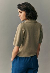 Kortärmad, olivgrön stickad tröja med krage, tillsammans med högmidjade blå denimbyxor. Mjuk textur, avslappnad passform.