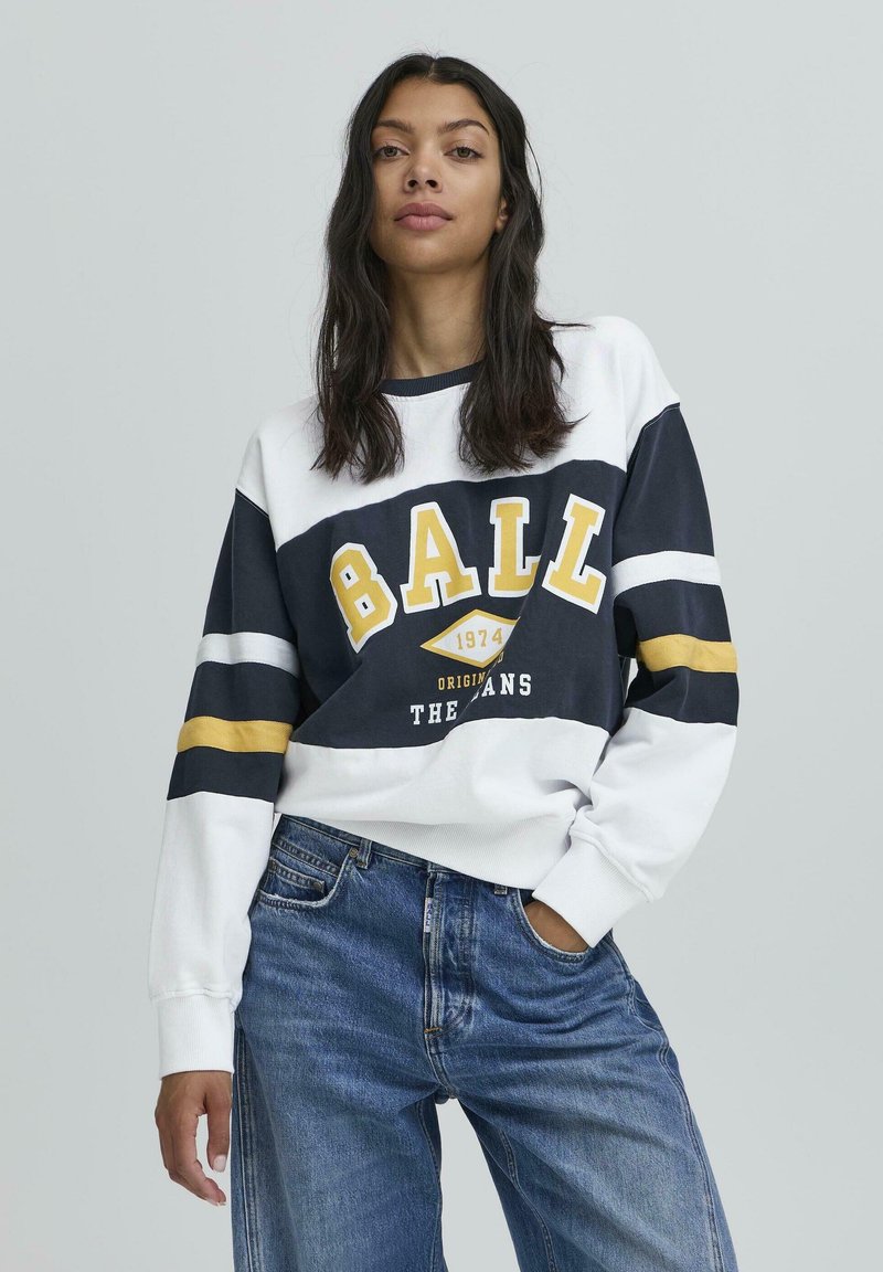Pulover alb și navy cu accente galbene. Are un grafic mare "BALL", 1974 și textul "THE ORIGINALS". Croi lejer, cu manșete ribbate.