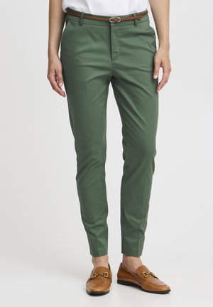 Green tailored trousers made of a smooth fabric, featuring a flat front and a slim fit, complemented by a brown belt and brown loafers.