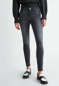 Jeans ajustados en denim gris oscuro con una textura suave y un ligero desgaste. Combinados con mocasines en blanco y negro que presentan acentos dorados.