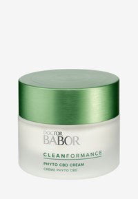 Tarro de vidrio blanco con una tapa de metal verde, etiquetado "Doctor Babor Cleanformance Phyto CBD Cream." Superficie suave y diseño moderno.