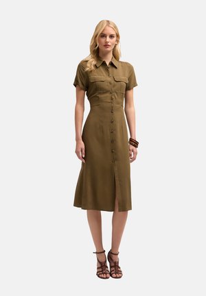 Olive green dress with short sleeves, button-down front, two chest pockets, knee-length hem, and side slit; worn with black strappy sandals.