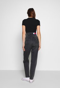 Černé džíny s vysokým pasem v uvolněném střihu, vybavené zadními kapsami a detaily na pásu s logem. V kombinaci s bílými teniskami.