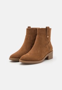 Braune Wildleder-Ankle-Boots mit spitzem Zehenbereich und Blockabsatz. Verfügt über eine flache Sohle und Ziehlaschen an den Seiten für leichtes An- und Ausziehen.