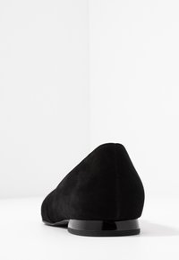 Zapato plano de ante negro con punta afilada y tacón negro brillante, que presenta una textura suave y un diseño minimalista.