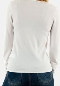 Valkoinen pitkähiha neuletoppi kevyestä kankaasta, jossa on istuva muotoilu ja tasosaumos, yhdistetty tummansinisisiin farkkuihin, joissa on taskut.