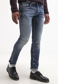 Miesten slim-fit-farkut vaalean ja tumman sinisen liukuvärjäyksellä, denimiä. Yhdistetty mustiin juhlakengiin ja harmaisiin käännettyihin lahkeisiin. Hienovaraiset haalistumat.