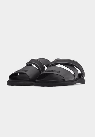 Sandales Moschino noires avec deux brides sur le pied, bout ouvert et semelle plate, vues de face en angle sur fond blanc.