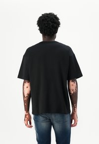 T-shirt en coton noir à manches courtes et coupe décontractée, avec un col rond et un design uni. Porté avec un jean en denim bleu.