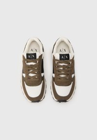 Pár bielych a hnedých tenísk Armani Exchange s čiernymi akcentmi, z sieťoviny, so šnúrkami na bielom pozadí.