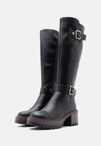Bottes noires en cuir montant jusqu'au genou avec un talon épais, dotées d'une fermeture éclair sur le côté et d'accents de boucles réglables. Semelles texturées pour une meilleure adhérence.
