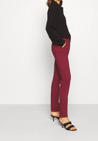Blouse noire à manches longues assortie à un pantalon slim bordeaux et des sandales à talons hauts noires à lanières. Tissu lisse et design ajusté.