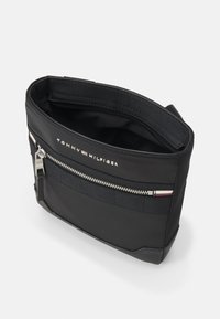 Borsa in nylon nera con cerniera argentata, tasca frontale con cerniera e accentuazione in tessuto a righe. Caratterizzata da una superficie liscia e un design strutturato.
