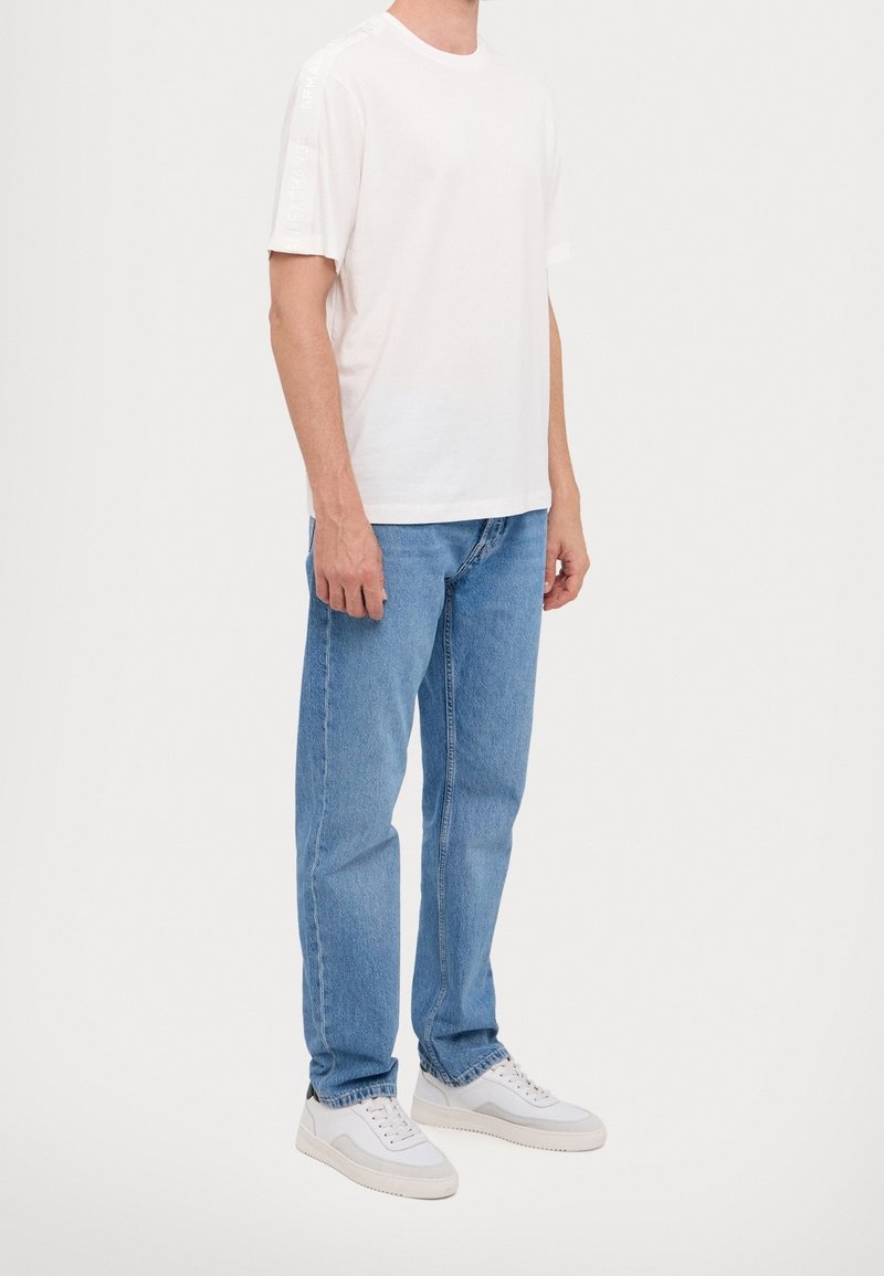 T-shirt en coton blanc à manches courtes, associé à un jean en denim bleu clair et des baskets blanches, mettant en valeur une coupe décontractée et un design simple.