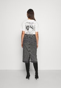 Valkoinen t-paita, jossa on graafinen kuvasto, joka esittää kuuta ja tekstiä; yhdistetty pitkään harmaaseen farkkuhameeseen, jossa on takareikä ja taskut. Mustat polvisukat.