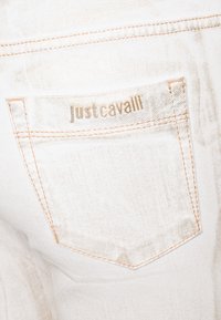 Vita denimjeans med en bakficka med en synlig logotyp "justcavalli" i metallisk skrift och kontrasterande sömdetaljer.