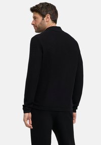 Maglione nero a maglia con orlo e polsini a coste. Presenta un collo classico e una silhouette aderente. Tessuto semplice, dettagli minimi.