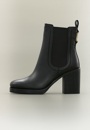 Bottine en cuir noir avec talon bloc, panneau latéral élastique et languette de tirage sur un fond clair uni.