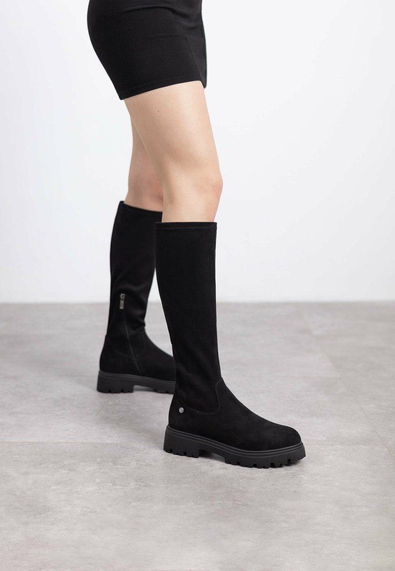 Stivali neri alti fino al ginocchio in suede con suola in gomma piatta. Presentano una cerniera laterale e una punta arrotondata. Finitura testurizzata in tutta la superficie.