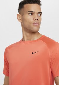 Nike trening T-skjorte i lys korall, laget av et teksturert, fukttransporterende stoff; har en svart logo på brystet og raglanermer.
