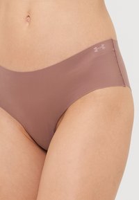 Culottes marron sans couture avec une taille basse, fabriquées en tissu doux. Elles présentent des coutures minimales et un logo discret sur la ceinture.