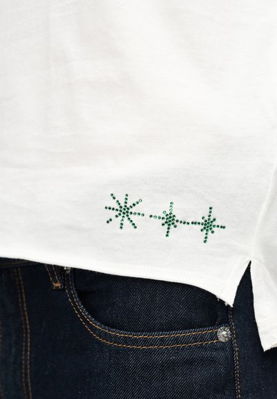 Λευκό βαμβακερό μπλουζάκι με πράσινες αστραφτερές αστέρια από στρας στο κάτω αριστερό μέρος, με στρογγυλεμένη ραφή και πλαϊνές σχισμές για άνεση.
