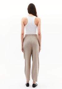 Pantalons beige à jambes larges avec texture à côtes verticales, taille élastique et coupe décontractée, associés à un haut sans manches blanc et des chaussures noires.