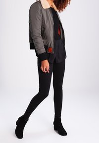 Olivgrön bomberjacka med pälskrage, quiltad textur och ribbade muddar, kombinerad med svarta skinny jeans och svarta ankelboots.