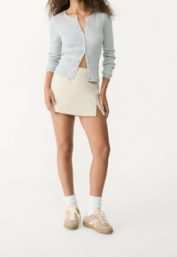 Jasnoszary prążkowany kardigan na guziki, beżowa mini spódnica z bocznym rozcięciem oraz beżowe trampki z białymi akcentami i białe skarpetki.