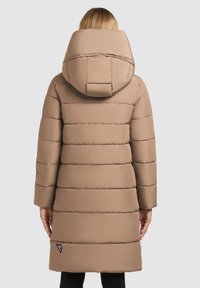 Lang, beige pufferjakke med hætte, der har vandrette quiltede sektioner, glat tekstur og et logo-patch på nederste venstre side.