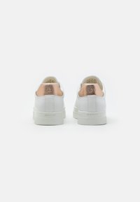 White sneakers with a smooth leather upper, rose gold accent at the heel, and a textured rubber sole. Brand logo displayed on back.