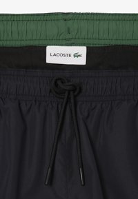 Pantaloni da nuoto neri realizzati in tessuto leggero con vita elastica, fodera interna verde a contrasto e lacci neri per una vestibilità regolabile.