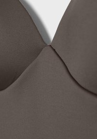 Gros plan d'une coque de soutien-gorge rembourrée marron foncé sans couture, avec un tissu lisse et une couture centrale reliant les bonnets.
