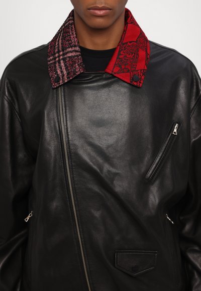 Black leather jacket with asymmetric zipper, contrasting red and plaid collar, and a zip pocket on the left chest. Smooth texture.