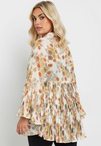 Floral blouse with a cream base, featuring orange, brown, and yellow leaf patterns. Pleated sleeves and back, lightweight fabric.