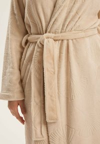 Beżowy pluszowy szlafrok z wytłoczonymi wzorami muszelek, z paskiem w talii, z długimi rękawami i miękkim, teksturowanym wykończeniem.