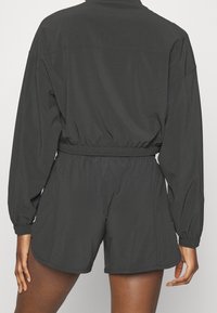 Mörkgrå jumpsuit med långa ärmar, elastisk midja och shorts. Tillverkad av ett mjukt tyg med minimala sömnadsdetaljer.