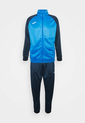 Träningsoverall bestående av en blå zip-up jacka med marinblå ärmar och byxor, tillverkad av ett mjukt tyg, med en logotyp på jackan och byxorna.
