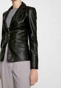 Černé kožené sako s přiléhavým střihem, ostrým límcem a zipovým uzávěrem. Nosit přes pruhované tričko, v kombinaci se světle šedými kalhotami.